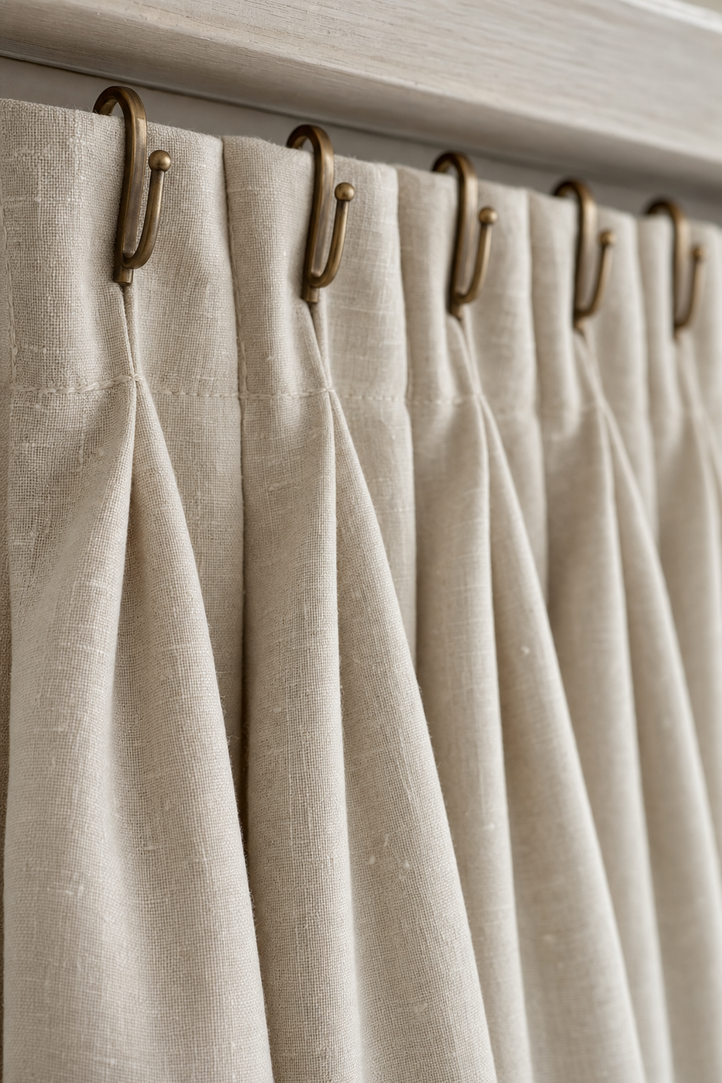 Close-up of pinch-pleat header on heritage ivory linen drapery with brushed-bronze hooks