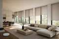 Open-plan living room with eight motorized greige roller shades lowered to varying heights