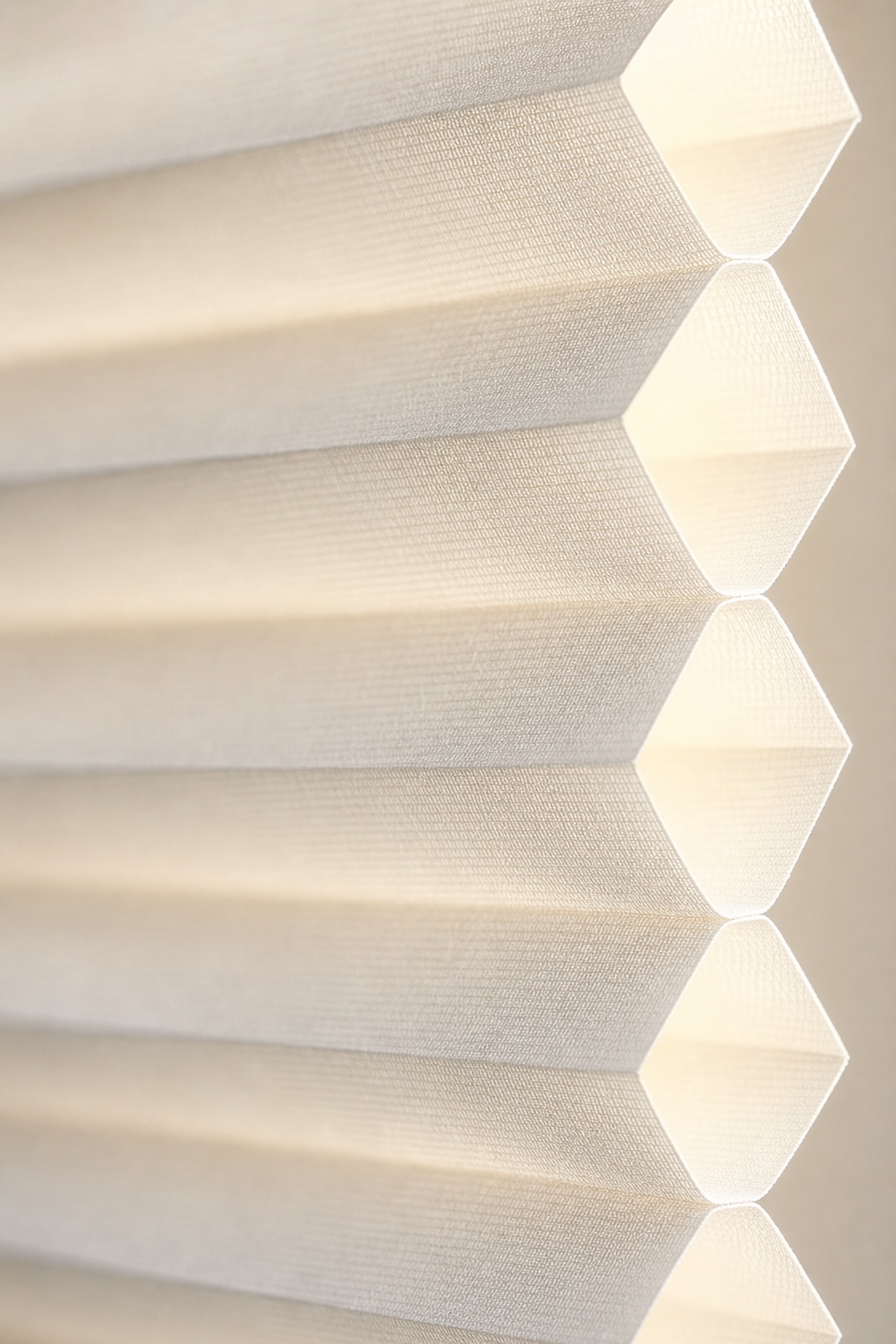 Close-up detail of a white double-cell honeycomb shade fabric backlit by warm light